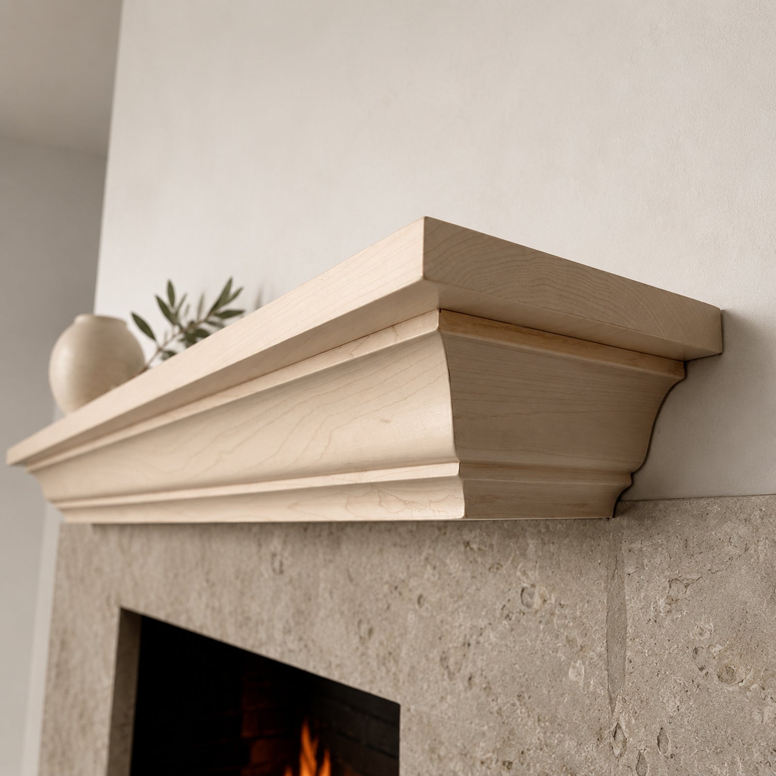 A light natural wood mantel shelf mounted above a stone fireplace, shown in a real interior setting with a vase and greenery on top.