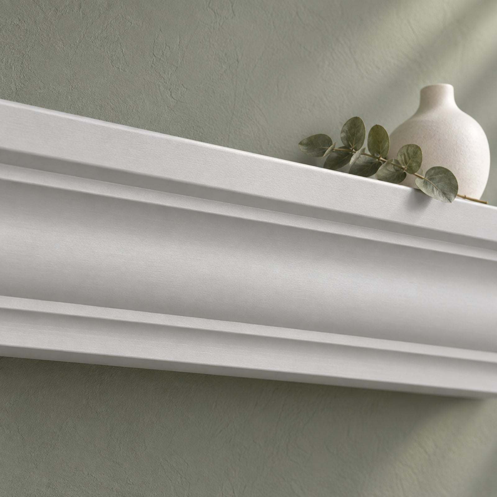 A close-up of a harbor gray floating mantel shelf on a textured sage green wall, with a small white vase and eucalyptus sprig resting on top.