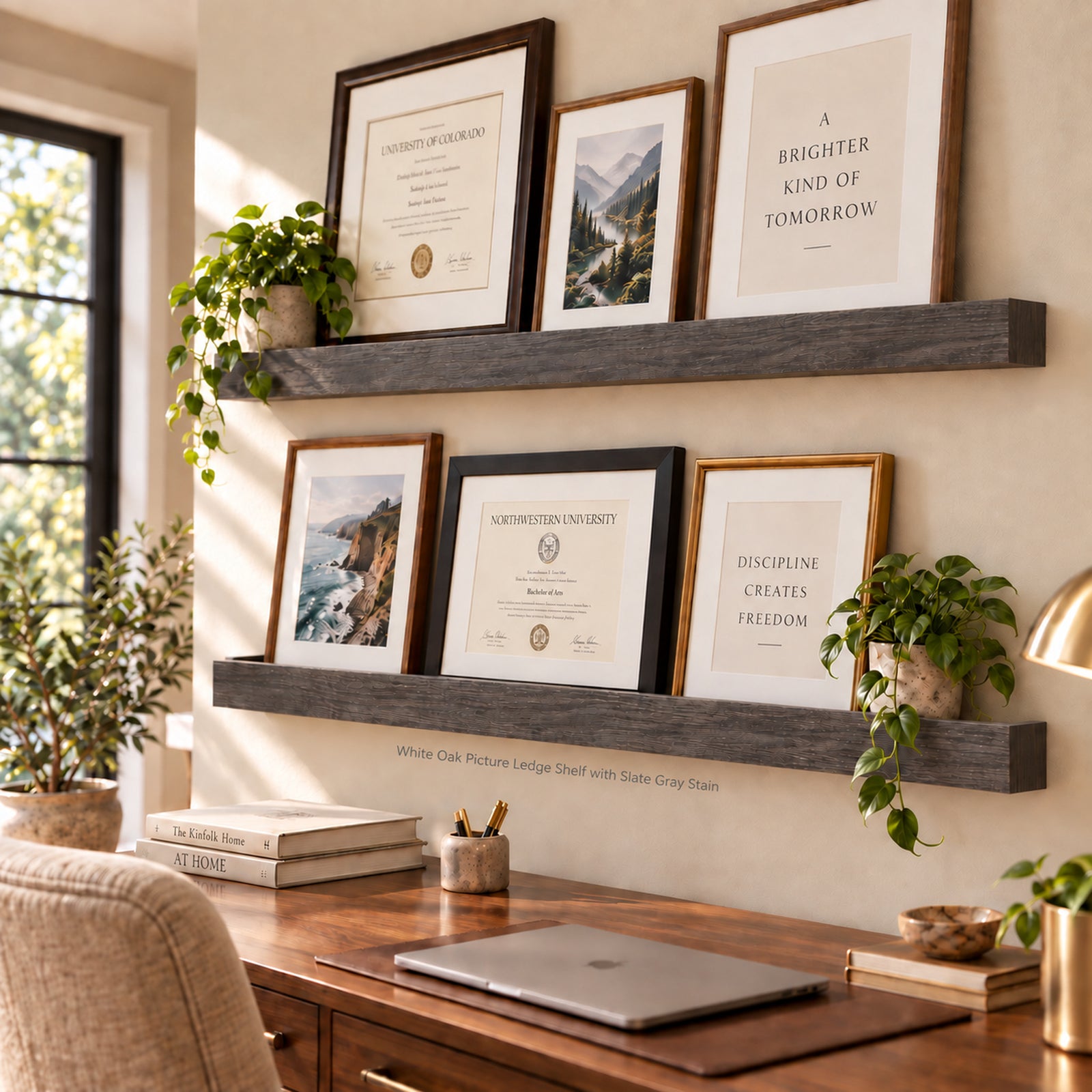 A styled home office scene showing two dark gray wooden ledge shelves mounted on a beige wall. The shelves display framed certificates, art prints, and motivational quotes, with potted green plants draped over them.