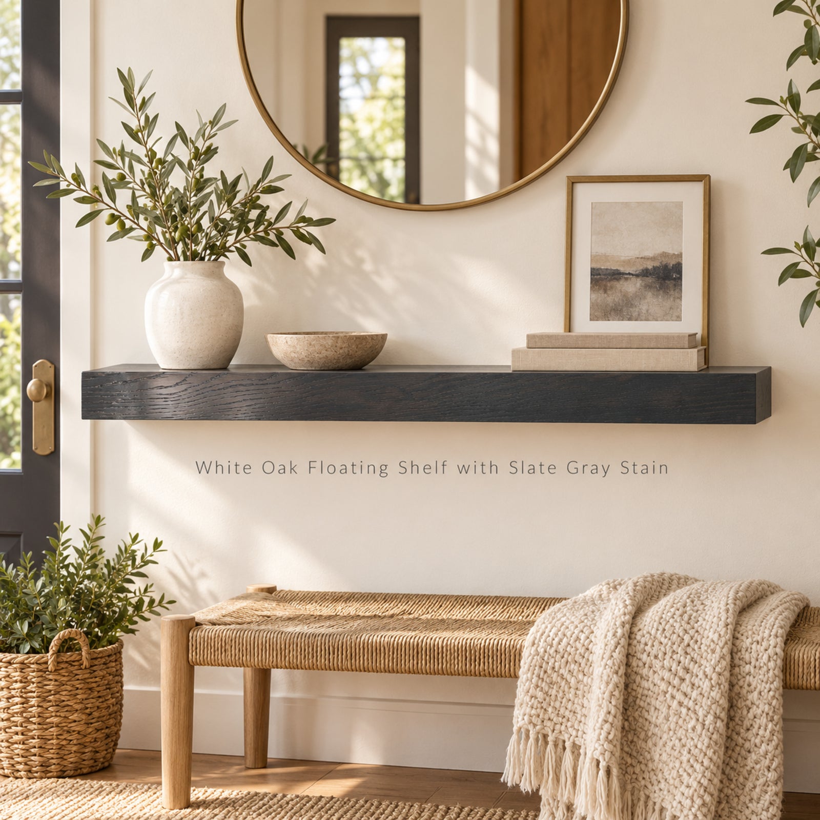 A floating shelf mounted on a cream wall in a styled entryway. The shelf is dark gray stained white oak wood and holds a white ceramic vase with greenery, a small stone bowl, and a framed print.