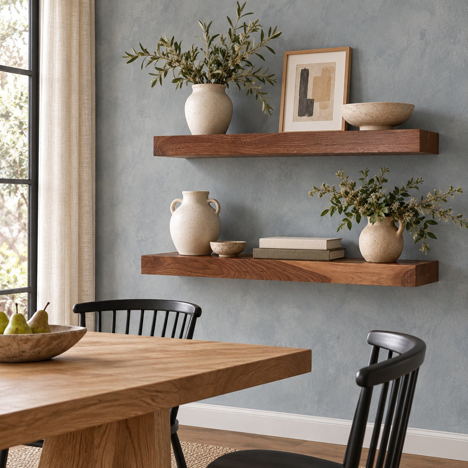 Two floating wooden shelves mounted on a textured blue-gray wall in a dining room setting, styled with ceramic vases, books, a bowl, and framed art.