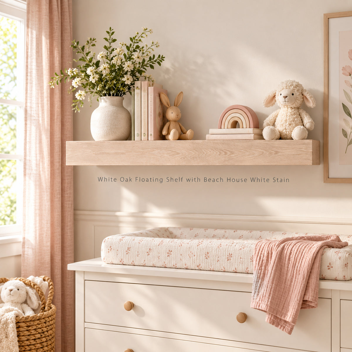 A floating wooden shelf mounted on a cream wall above a white changing dresser. The shelf is styled with a ceramic vase of white flowers, books, a small rabbit toy, a pastel rainbow, and a plush sheep.