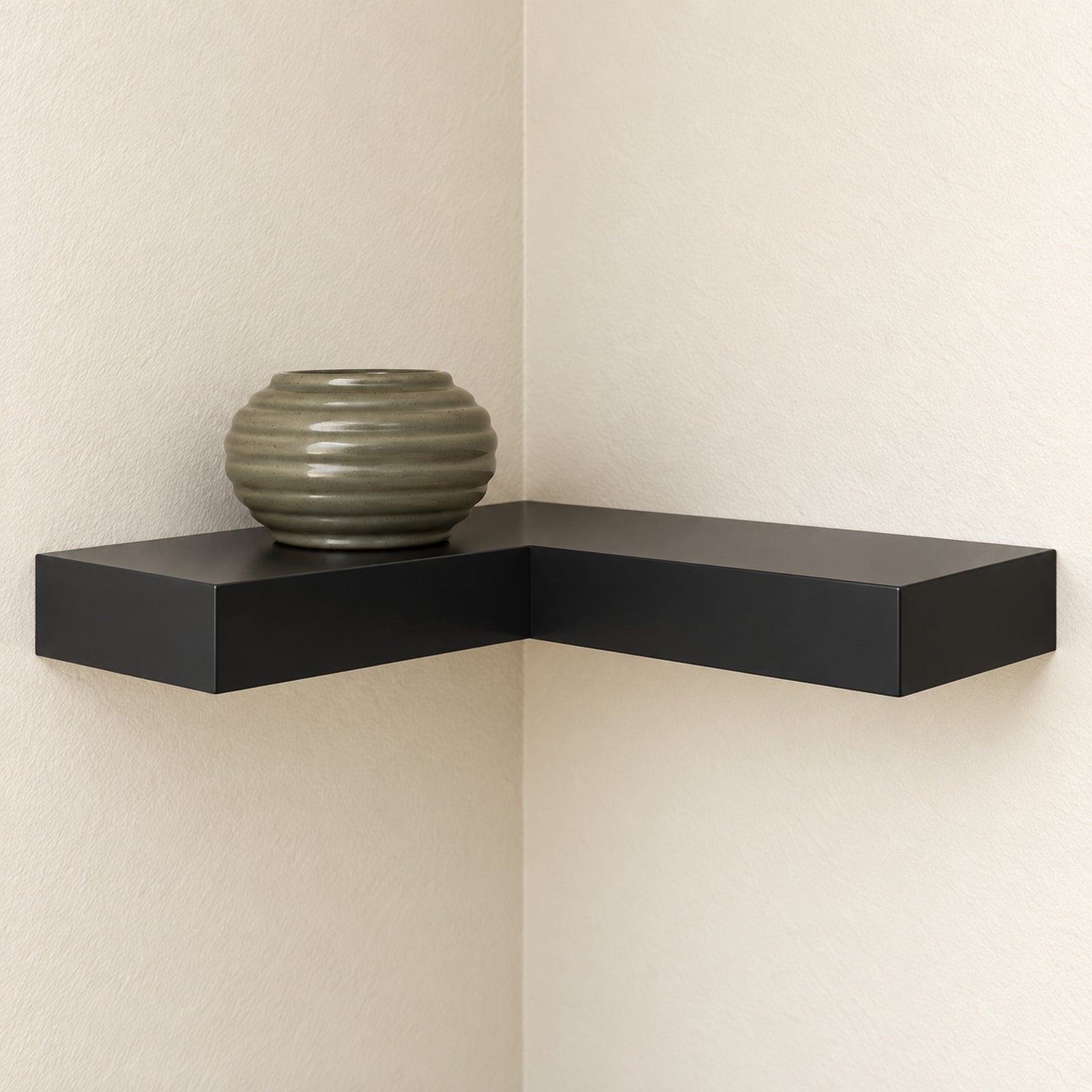 A modern black L-shaped floating corner shelf mounted on two cream-colored textured walls, holding a ribbed olive-green ceramic vase.