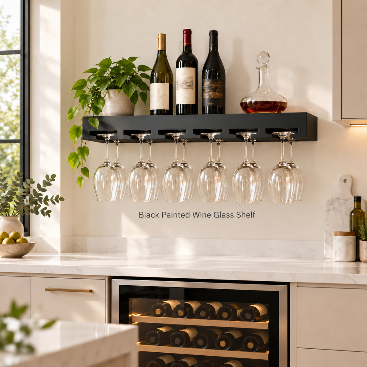 A black wall-mounted floating wine glass shelf in a modern kitchen setting, holding several wine bottles and a decanter on top and five clear wine glasses hanging below. The shelf is mounted on a white backsplash wall above a wine cooler.