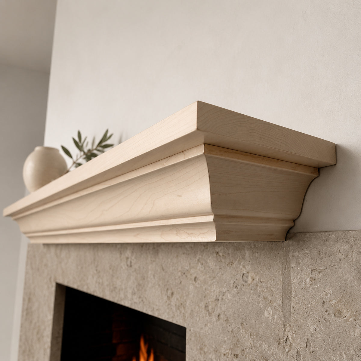 A light natural wood mantel shelf mounted above a stone fireplace, shown in a real interior setting with a vase and greenery on top.