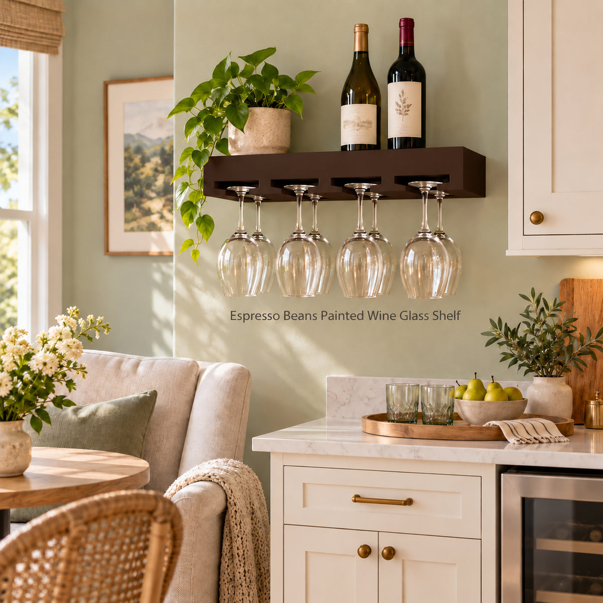 A wall-mounted espresso beans painted  shelf in a warm kitchen setting, holding two wine bottles and eight inverted wine glasses. The floating shelf is mounted on a sage green wall above a white cabinet, with decorative plants and a framed picture nearby.