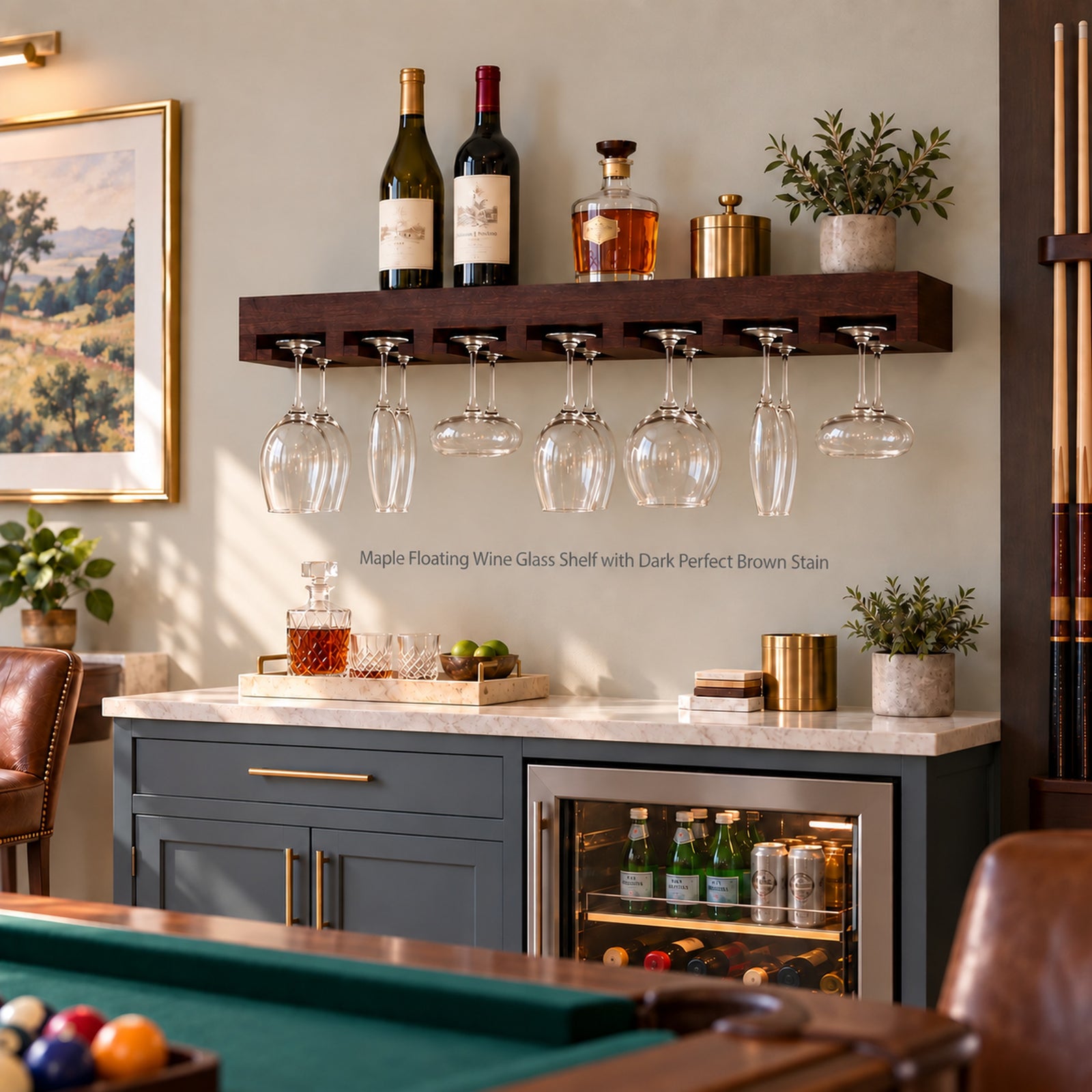 A dark brown floating wine glass shelf mounted on a wall in a home bar setting, holding wine bottles and fourteen hanging clear wine glasses and other stemware. The shelf is shown in a styled interior with a marble countertop, blue-gray cabinets, and a pool table edge visible in the foreground.