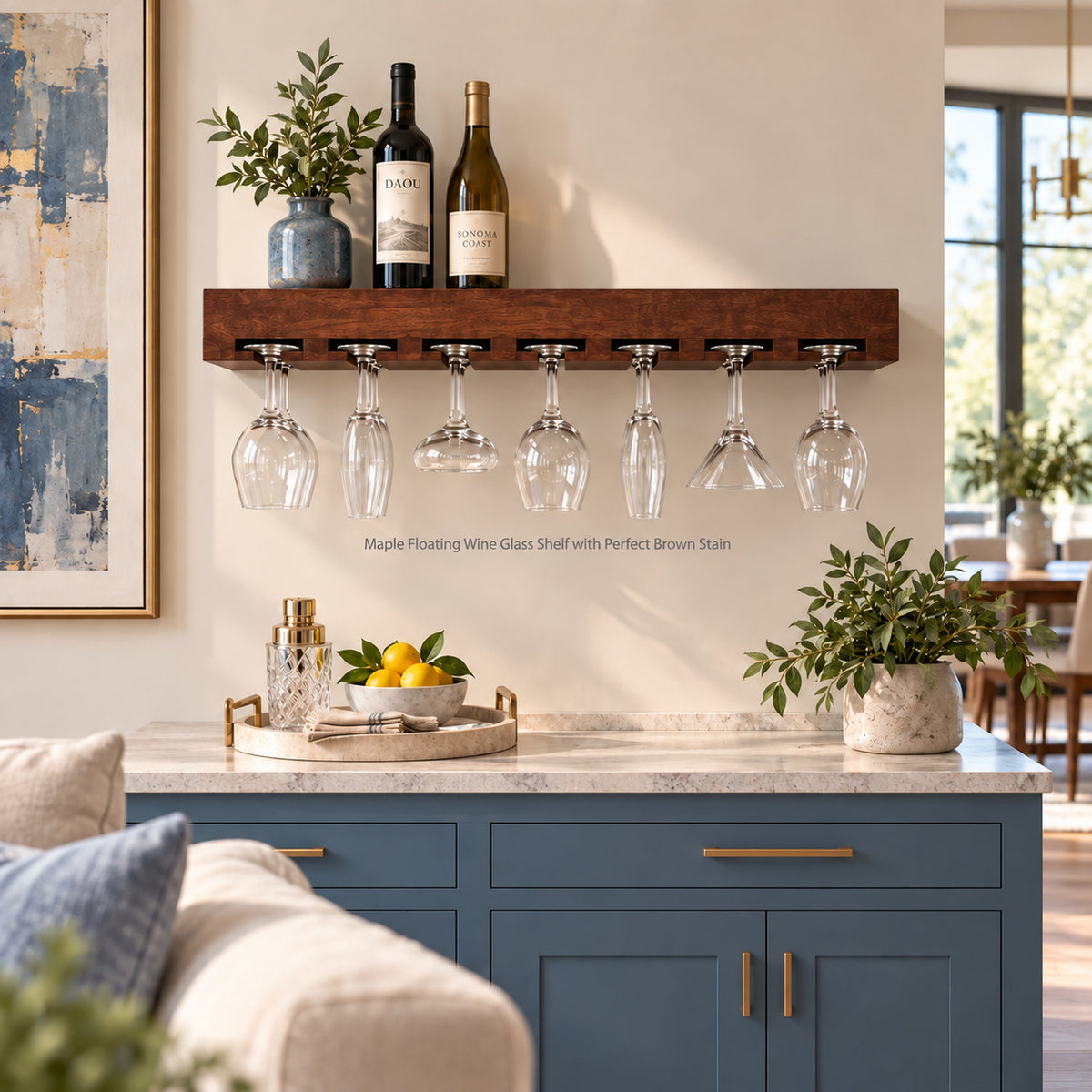 A dark brown wooden floating wine glass shelf mounted on a beige wall above a blue kitchen cabinet. The shelf holds two wine bottles and fourteen wine glasses and other stemware hanging from its floating slots.