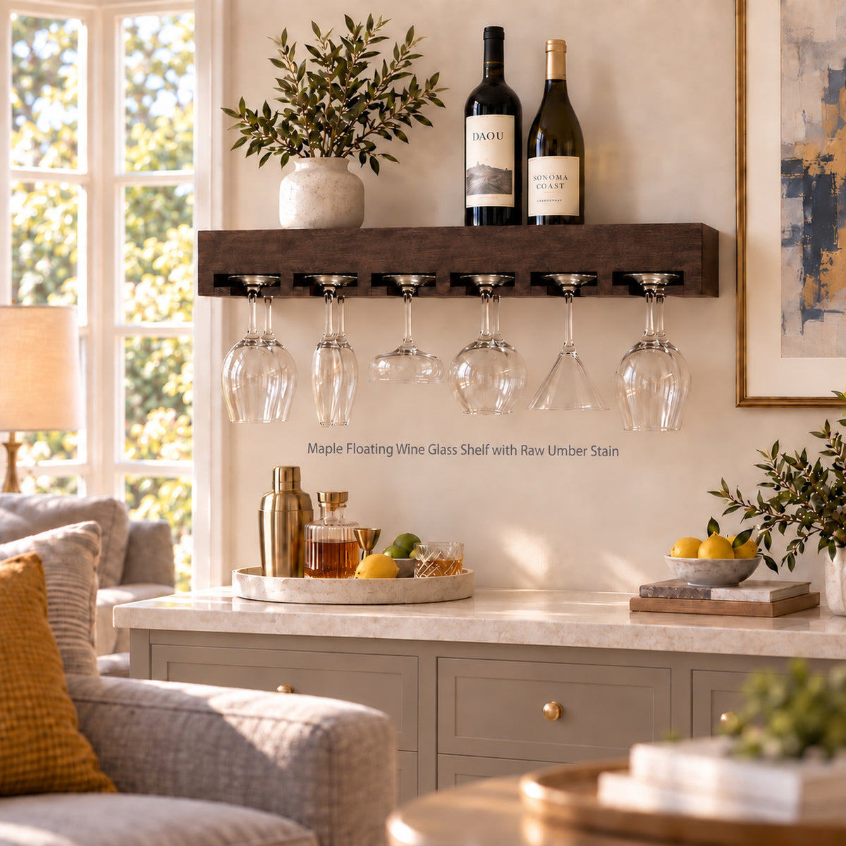 A floating wine glass shelf mounted on a beige wall in a bright living room. The dark wood floating shelf holds two wine bottles on top and twelve hanging wine glasses and other stemware.