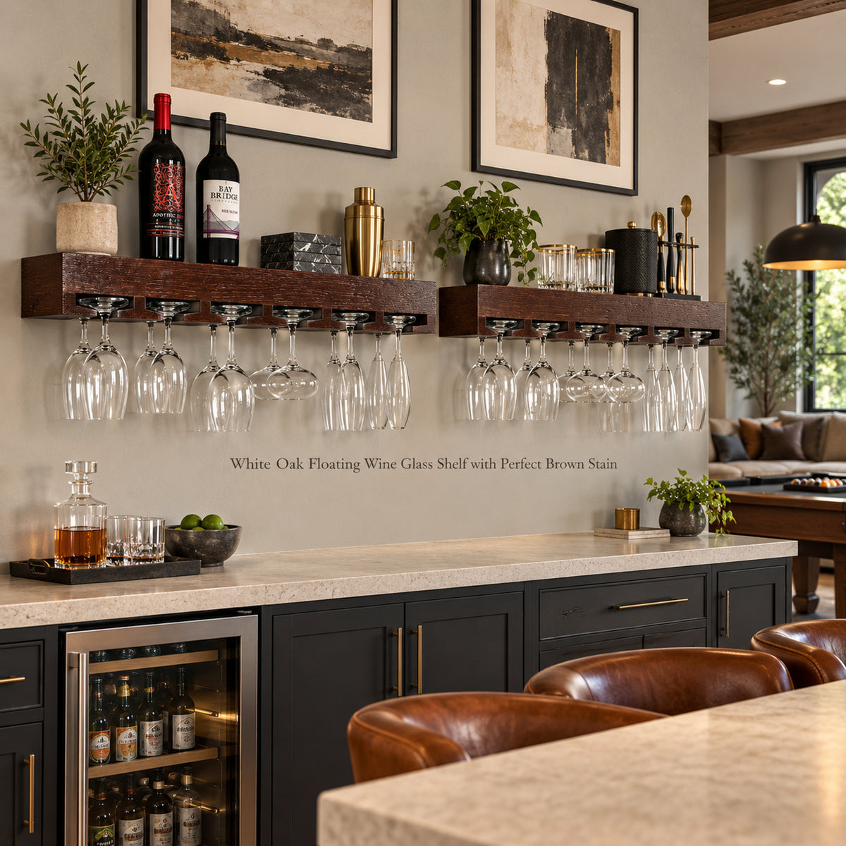 Two dark brown floating wine glass shelves mounted on a beige wall above a bar counter, holding wine glasses, stemware and bar accessories, with framed wall art and a modern home interior in the background.