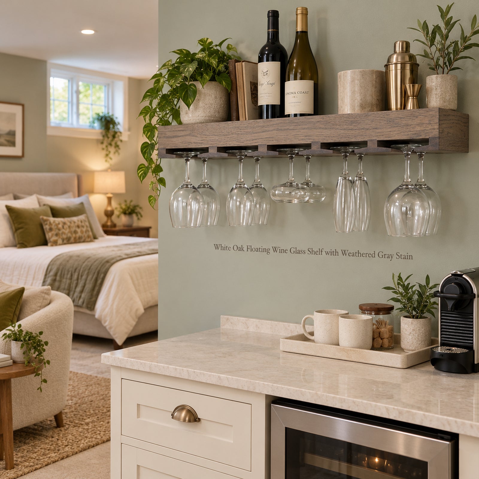 A floating wooden wine glass rack mounted on a sage green wall in a modern bedroom/living space. The rack holds several ten glasses hanging upside down, with wine bottles, books, and plants displayed on the shelf above.